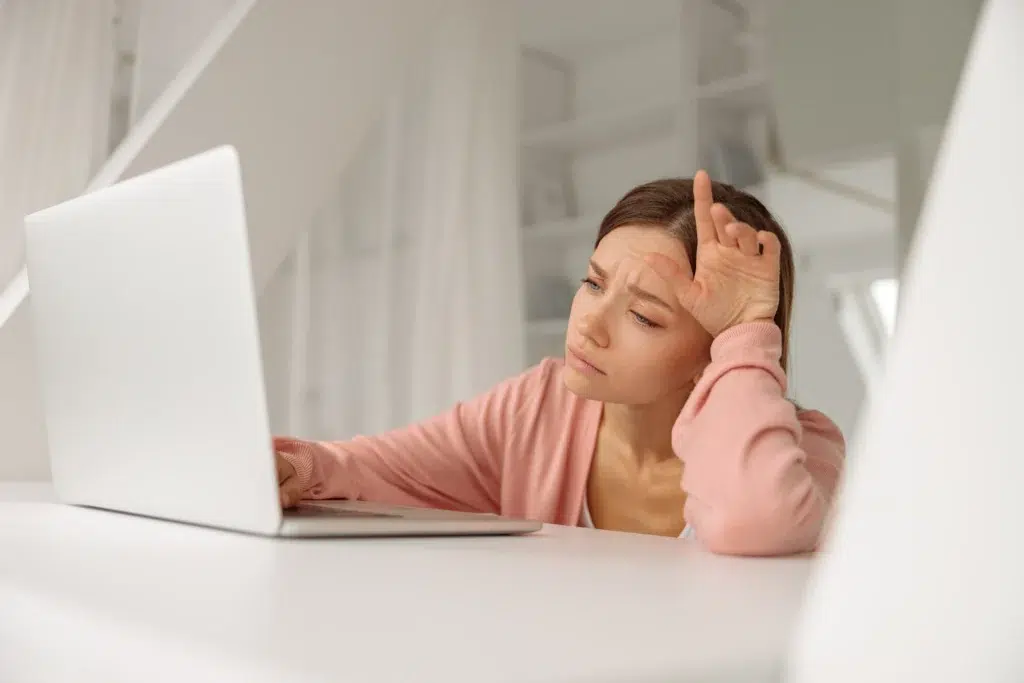 A tired young founder stares blankly at her laptop screen, demonstrating the 'Burnout Bottleneck' where mental fatigue stalls small business productivity. This image illustrates the stage where learning how to recover from burnout while still working requires radical delegation