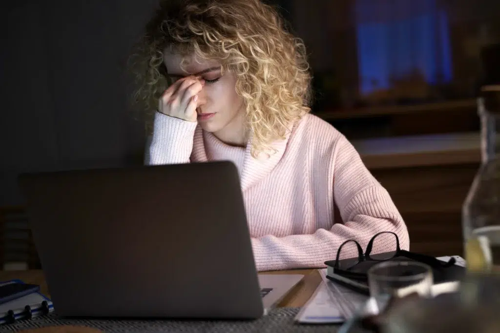 An exhausted woman working late at night covers her eyes in stress, visualizing the tipping point for an overwhelmed entrepreneur. This image represents the hidden cost of doing everything yourself and the moment a leader must consider a virtual assistant for small business to reclaim operational sanity